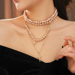 Detail of layered gold cross necklaces and pink pearl choker on a woman's neck