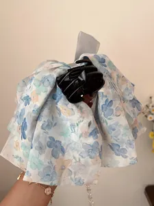 Détail d'une pince à cheveux avec nœud en mousseline fleurie bleue et gravure artisanale