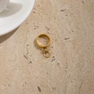 Detail of minimalist gold-plated stainless steel ring with OT buckle charm on stone surface