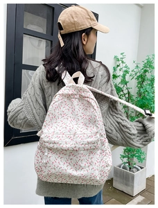 Detail of floral canvas backpack with beige straps shown on a model's back outdoors
