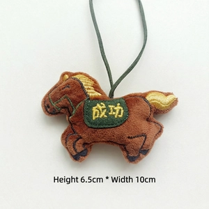Detail of plush horse charm with green saddle and golden 'Success' embroidery