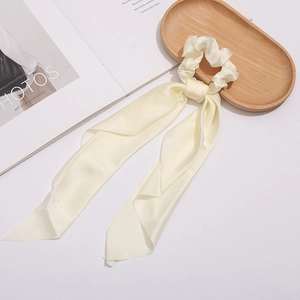 Detail view of a cream satin scrunchie with long ribbons on an aesthetic wooden tray