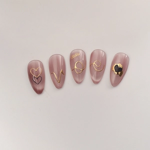 Close-up of pink cat-eye press-on nails with 5D embossed gold LOVE and heart art