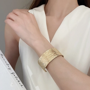 Detail of wide open gold cuff bracelet with textured hammered metal finish on wrist