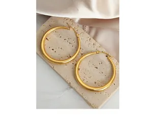 Detailed view of large gold titanium steel hoop earrings on a stone display surface