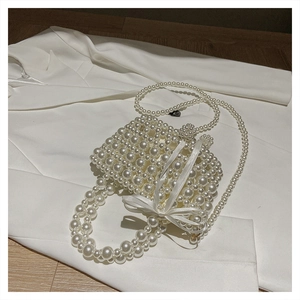 Détail du sac panier en perles avec nœud en soie sur fond de blazer blanc