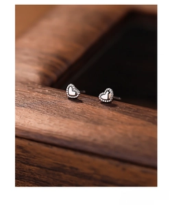 Close-up of heart-shaped S999 sterling silver stud earrings on a textured wooden background