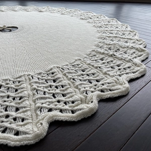 White knitted Christmas tree skirt with hollow wave edges on a dark wooden floor