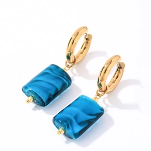 Detail of gold hoop earrings with translucent blue stone pendants and water-ripple texture