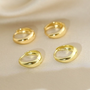 Set of two pairs of minimalist polished gold hoop earrings on beige silk fabric background