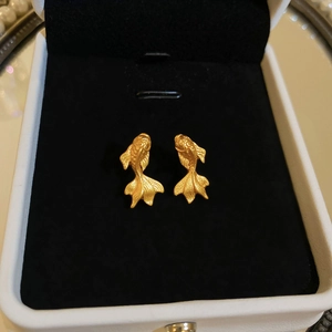 Detail shot of golden koi fish stud earrings on black velvet lining inside a jewelry box