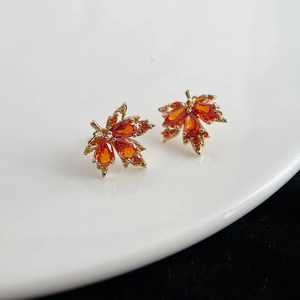 Détail de boucles d'oreilles feuille d'érable dorées avec zircons orange de coupe marquise