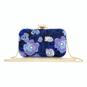 Detail of floral embroidery on navy blue clutch bag with pearl accents and gold hardware