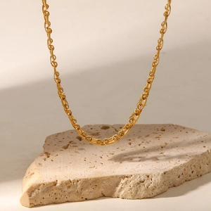 Vue détaillée d'un collier chaîne en titane plaqué or 18K sur fond de pierre décorative