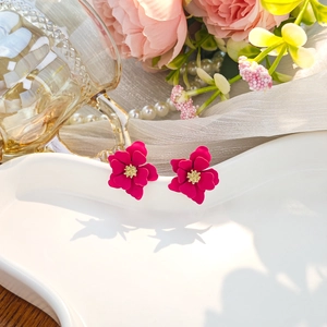 Macro detail of dark pink multi-layered flower earrings with golden core on ceramic tray