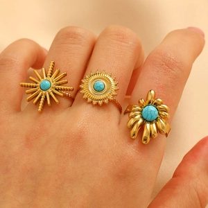 Detail of bohemian gold rings set with turquoise stones worn on hand against fabric