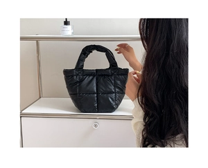 Detail of minimalist black quilted down tote bag on a white shelf in natural light
