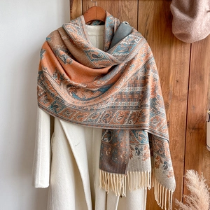 Detail of bohemian cashmere-like scarf with orange paisley patterns and tassel fringe edge