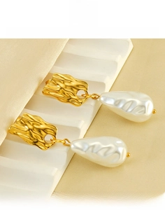 Détail de boucles d'oreilles dorées texturées avec perles baroques sur un support