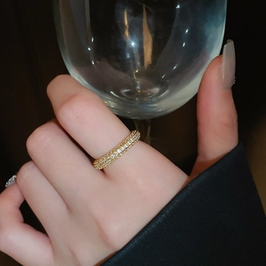 Close-up of a gold-plated twisted ring with pavé zircons worn by a model holding glass