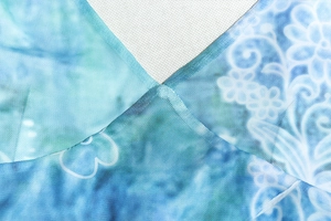 Close-up of blue-green tie-dye mesh fabric with precision stitching and floral print