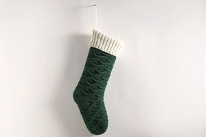 Detail of dark green knitted Christmas stocking with white cuff and fish scale texture