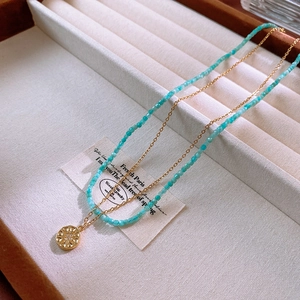 Detail of double-layer necklace with blue beads and a gold embossed pendant on a beige tray