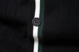 Dettaglio del cardigan in maglia nera con strisce verdi e bianche e bottone in resina