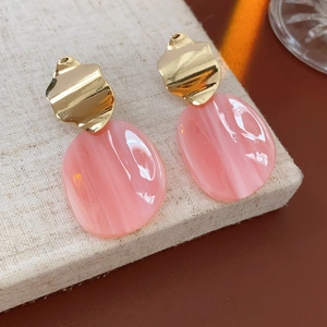 Détail de boucles d'oreilles en métal doré et acrylique rose sur un support en lin