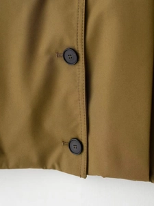 Dettaglio del tessuto in twill di cotone kaki con due bottoni neri e cuciture rifinite