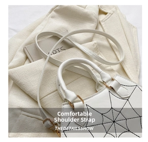 Detail of white PU handbag showing black spider web embroidery and gold hardware accents