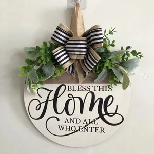 Detail of wooden door wreath with 'BLESS THIS HOME' text, green foliage, and striped bow