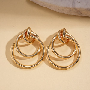 Detailed shot of golden geometric hollow metal earrings on a warm beige background