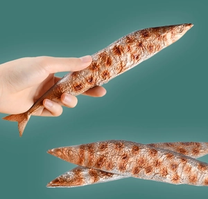 Close-up of realistic plush saury toy showing detailed grilled texture and hand-held scale