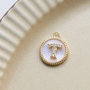 Macro detail of a gold letter T pendant with shimmering shell and zircon inlay