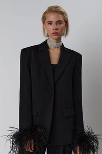 Detail of black blazer featuring luxurious feather cuffs and elegant rhinestone accessories