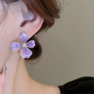 Close-up of a purple enamel flower earring with a white pearl center on a model's ear