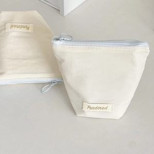 Detail view of cream makeup pouch with light blue zipper and Purdored fabric label