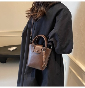 Brown leather bucket bag with top handle and braided knot charm worn with a black jacket