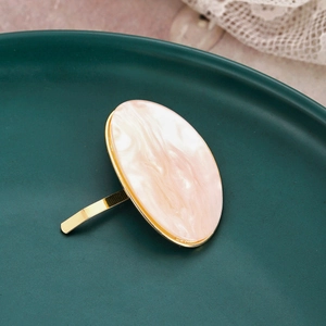 Detail shot of a gold-plated oval hair hook with pink marble pattern on a ceramic dish