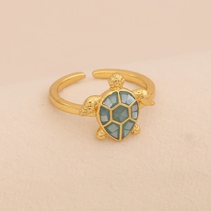 Close-up of golden sea turtle ring with turquoise shell inlay on beige fabric background