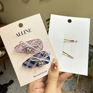 Detail of pink plaid hair clip with silver bow and heart pendant on paper card