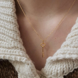 Close-up of vintage golden key necklace worn with a white textured knit sweater
