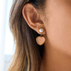 Pink heart-shaped 18K gold earrings with white pearl detail on a female model