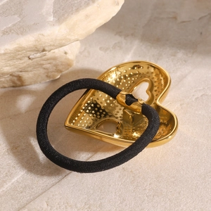 Golden heart hair tie with textured metal charm and black elastic on a stone surface