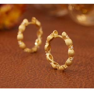 Macro detail of gold-brushed earrings with zircon inlay on dark leather background