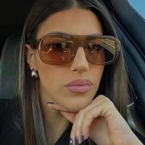 Close-up of oversized square sunglasses with amber frames worn by a model in a car