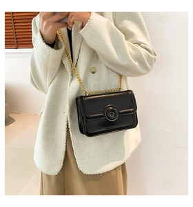 Detail of black rectangular crossbody bag with round metal buckle and gold chain strap