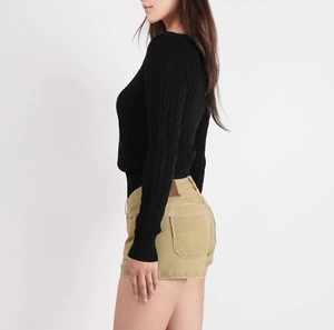 Detail of black cable knit sweater and khaki corduroy shorts on a side-view model