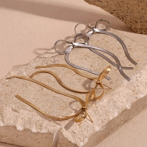 Close-up of gold and silver bow tassel earrings on a natural stone display